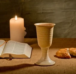 A glowing candle beside bread and wine, symbolizing the reflective nature of Holy Communion.