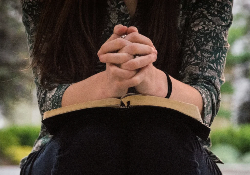 Clasped hands in prayer with an open Bible, symbolizing seeking God’s guidance in honouring parents.