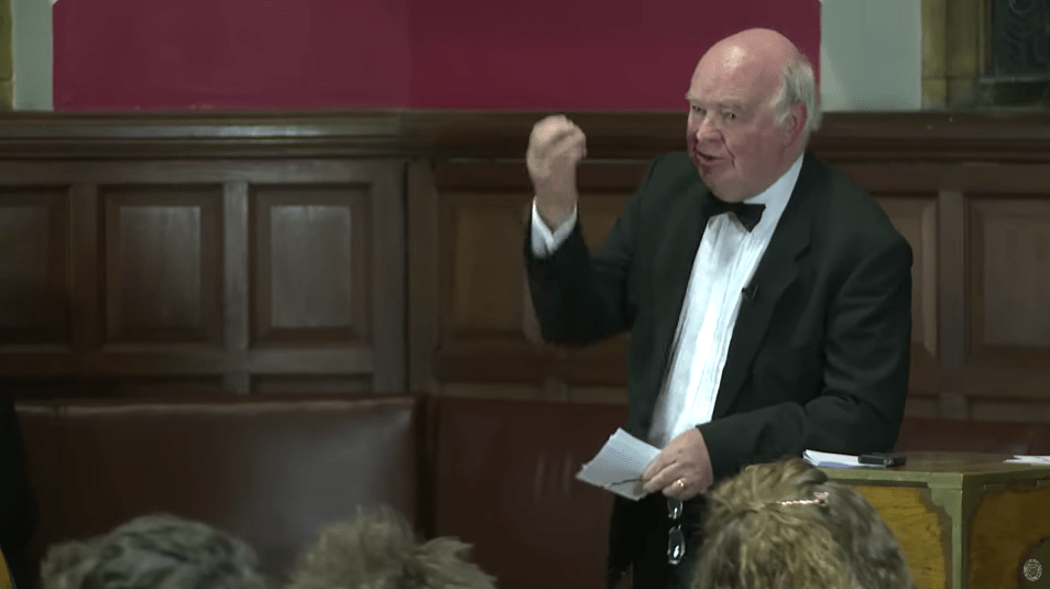 Professor John Lennox speaking passionately about the coexistence of faith and science during a discussion on God’s existence.